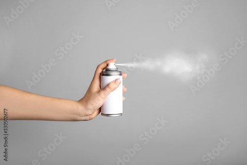 Woman holds spray can in hands on grey background