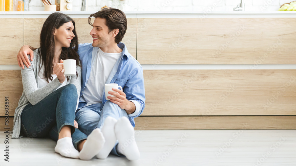 Young couple enjoying coffee, sitting on floor at kitchen Young couple enjoying coffee, sitting on floor at kitchen