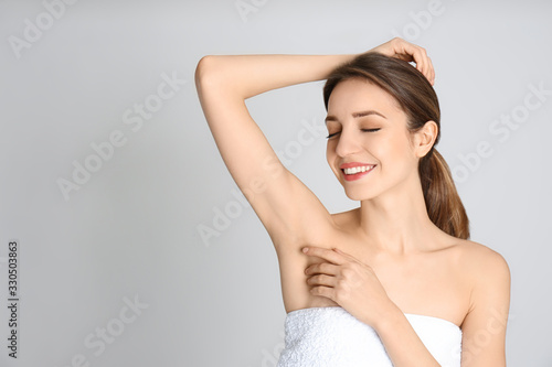 Young woman showing armpit with smooth clean skin on light grey background, space for text photo