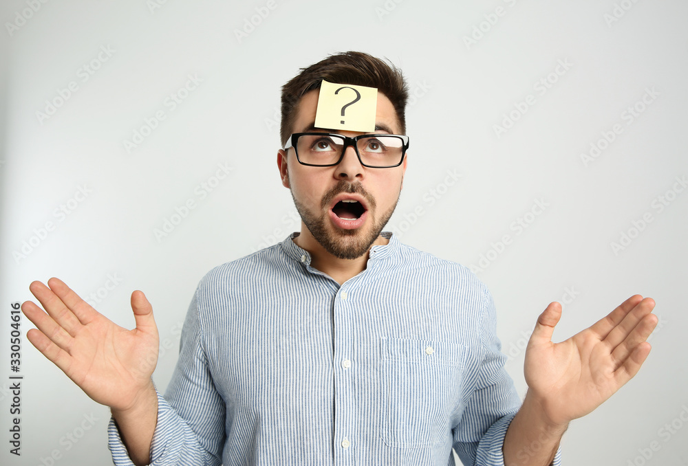 Emotional man with question mark sticker on forehead against light background Emotional man with question mark sticker on forehead against light background