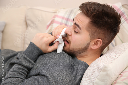 Sick young man sneezing at home. Influenza virus