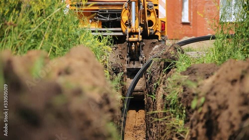 An excavator digs a trench for laying a cable. Summer sunny day. Excavator digs a trench for laying the cable