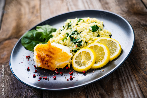 Risotto with fried cod on wooden background