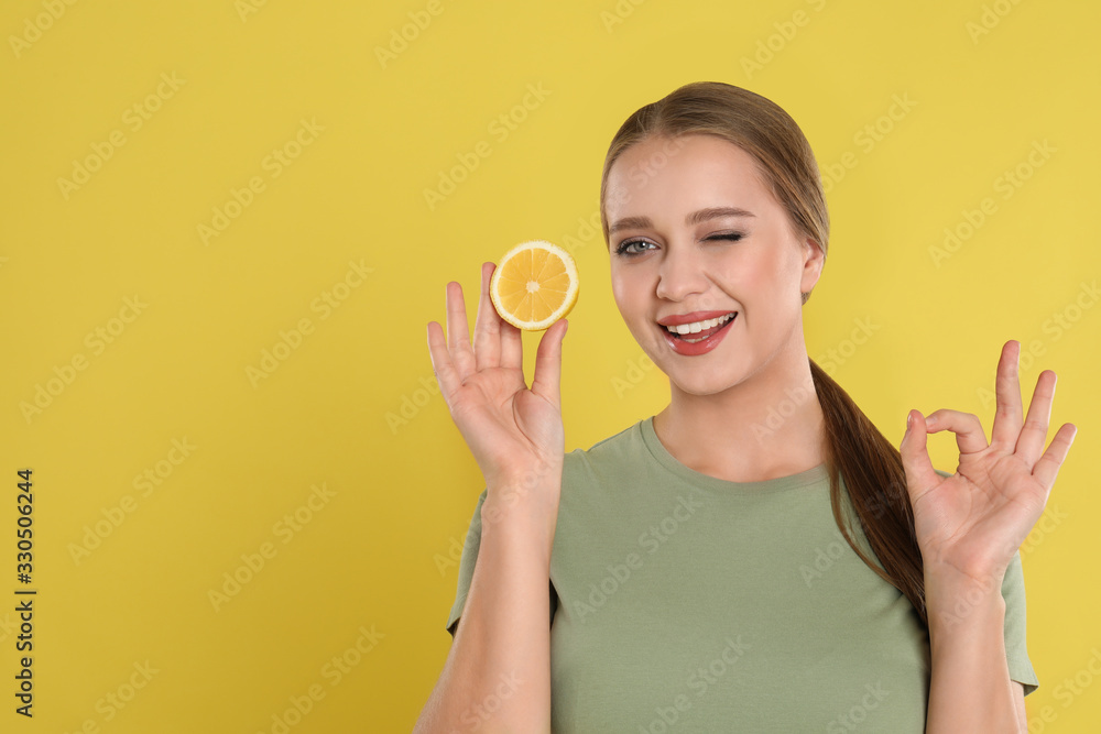 Young woman with cut lemon on yellow background, space for text. Vitamin rich food Young woman with cut lemon on yellow background, space for text. Vitamin rich food