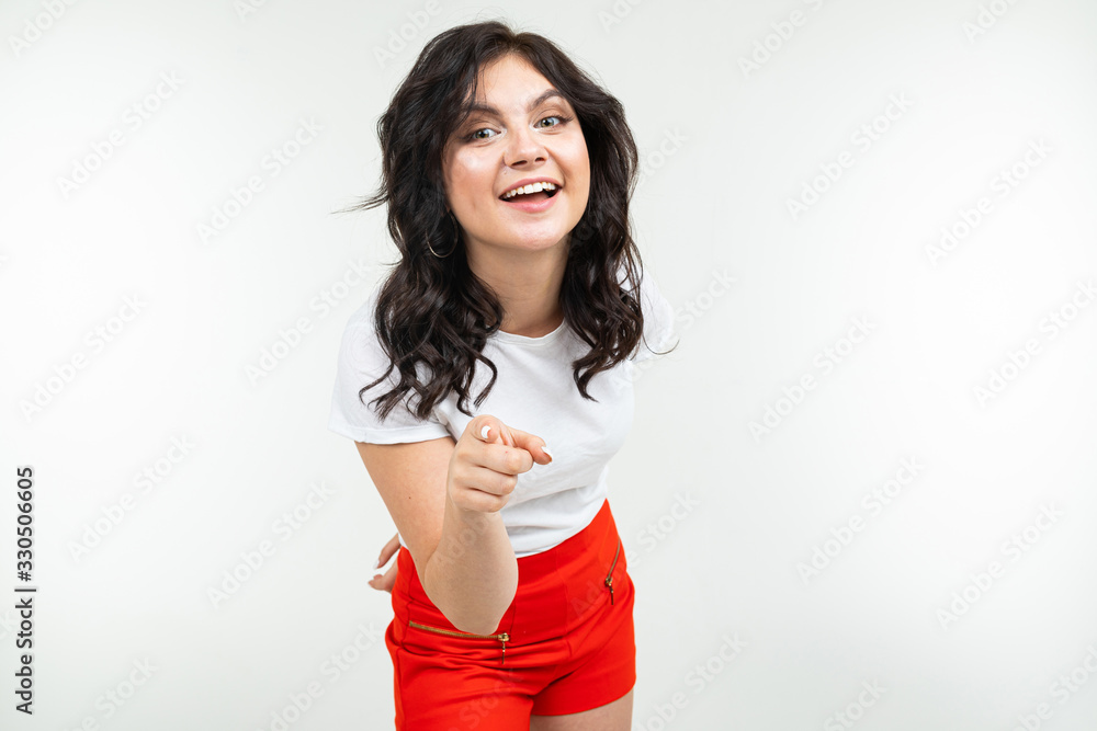 charming brunette in a white tank top and red trousers points her finger forward on a white background charming brunette in a white tank top and red trousers points her finger forward on a white background