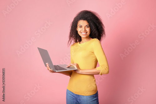 Young african woman with laptop on pink background © LumenSt