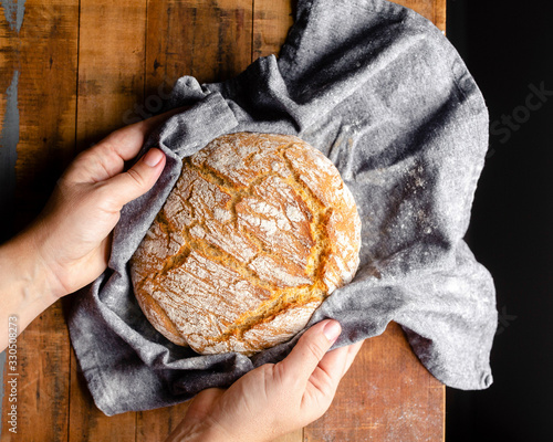 Hands placing a freshly baked loaf of bread wrapped in a grey cloth onto a wood tabletop. photo