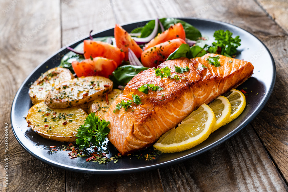Fried salmon steak with potatoes and vegetables on wooden table Fried salmon steak with potatoes and vegetables on wooden table