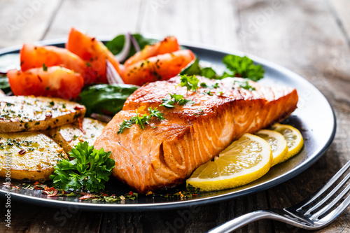 Fried salmon steak with potatoes and vegetables on wooden table