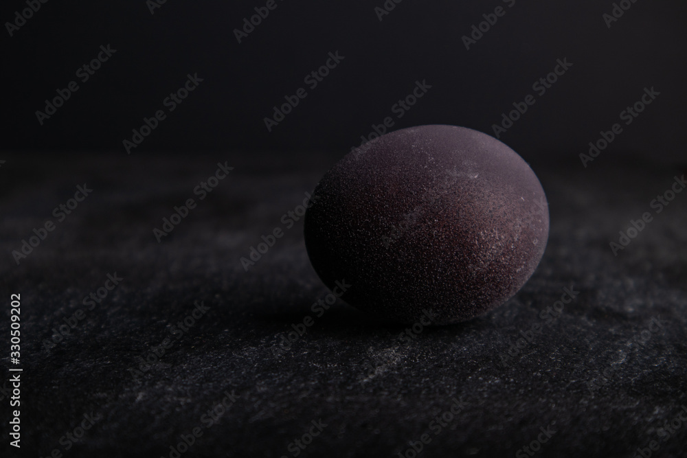 Close-up dark easter egg on stone table with black backdrop. Colored with wine. Close-up dark easter egg on stone table with black backdrop. Colored with wine.