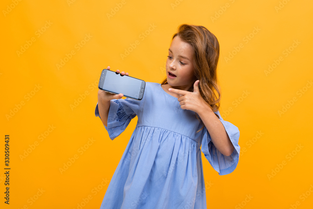 teenager girl in a blue dress holds the phone horizontally with a layout for the site on a yellow background teenager girl in a blue dress holds the phone horizontally with a layout for the site on a yellow background