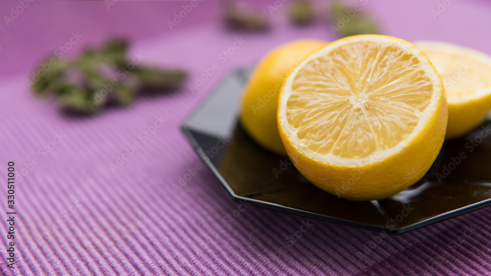 Halfs of ripe lemons, citrus, fruit on a black plate. Isolated on purple fabric background Halfs of ripe lemons, citrus, fruit on a black plate. Isolated on purple fabric background
