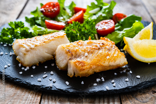 Photo Fish dish - fried cod fillet with vegetables on wooden table