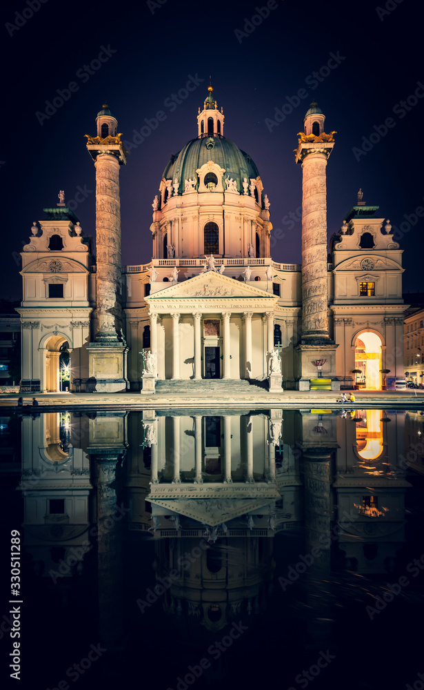Vertical image of Karslkirche church  buiding and its reflectios at night time with tourists sitting nearby. Toruism and historical buildings in Viena. Asutria.
