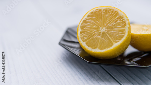 Half of ripe lemon, citrus, fruit on a black plate. Isolated on white wooden vinyl background