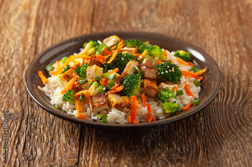 Tofu with rice and vegetables. Served on brown plate.