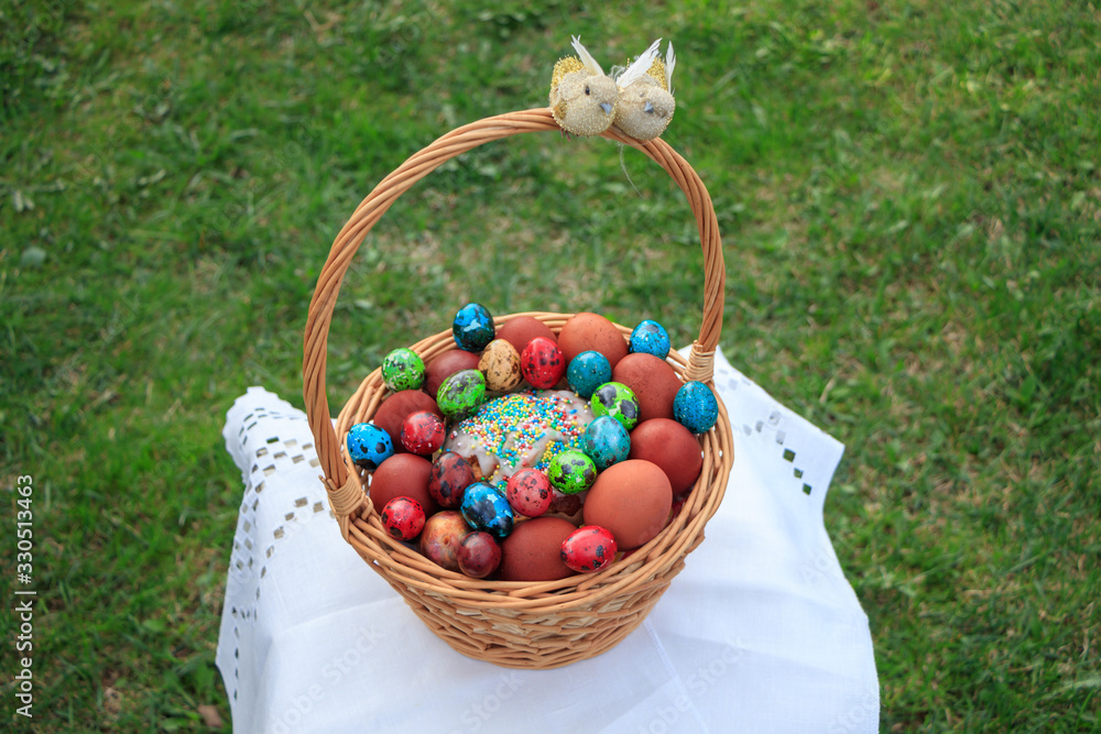Basket of twigs with Easter eggs painted in different colors and different sizes and Easter cake on a tablecloth