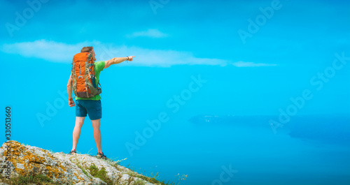 Man hiker with backpack points to the distant island © Bashkatov