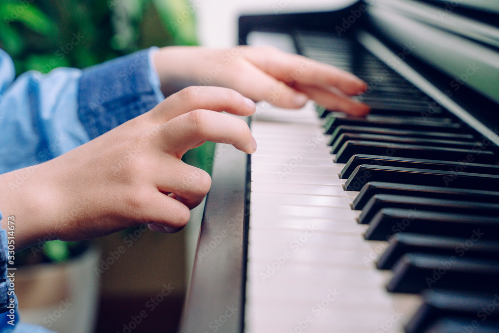 Obraz premium Unrecognizable child playing the piano. Detail of little boy hands touching a keyboard at home. Student of pianist musician rehearsing classical music. Educational music lifestyle.