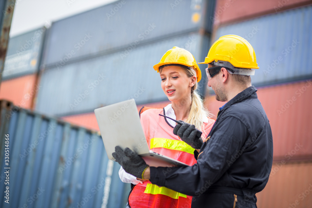 Female dock worker wearing a white helmet yellow standing in a industrial shipping yard she discussing colleagues and control container transportation and export with commercial docks. Female dock worker wearing a white helmet yellow standing in a industrial shipping yard she discussing colleagues and control container transportation and export with commercial docks.