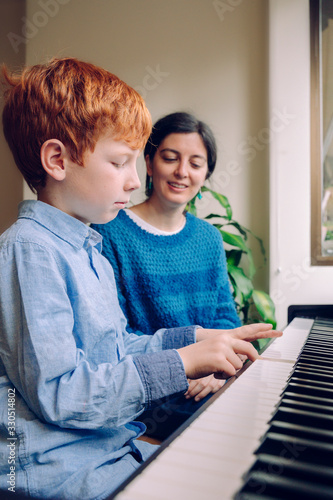 Children with musical virtue and artistic curiosity. Educational musical activities. Piano teacher woman teaching a little boy at home piano lessons. Family lifestyle spending time together indoors.