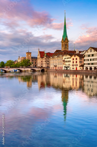 Famous Fraumunster church with reflections in river Limmat at pink sunrise in Old Town of Zurich, the largest city in Switzerland