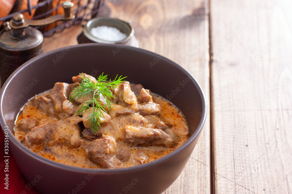 Traditional beef stroganoff in ceramic bowl on a wooden table, horizontal, copy space