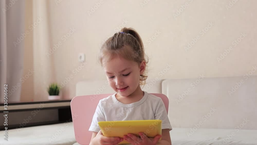 Four years little girl with pretty face girl using childrens digital tablet technology device sitting on chair near sofa. Four years little girl with pretty face girl using childrens digital tablet technology device sitting on chair near sofa.