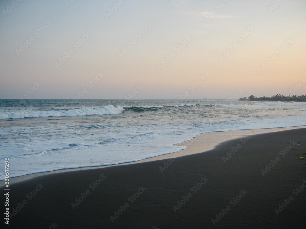 View of the black sands at sunset. The waves are chasing. Bali.