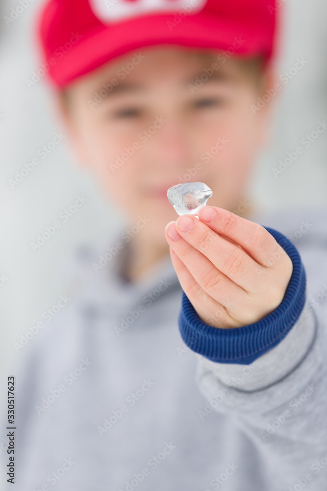 Young boy shows a little piece of ice in hand at winter time, outdoors. Young boy shows a little piece of ice in hand at winter time, outdoors.