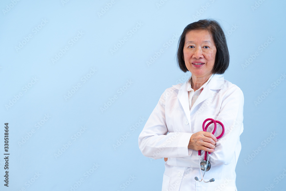 A beautiful old asian doctor holding stethoscope in hand, standng on the blue background A beautiful old asian doctor holding stethoscope in hand, standng on the blue background