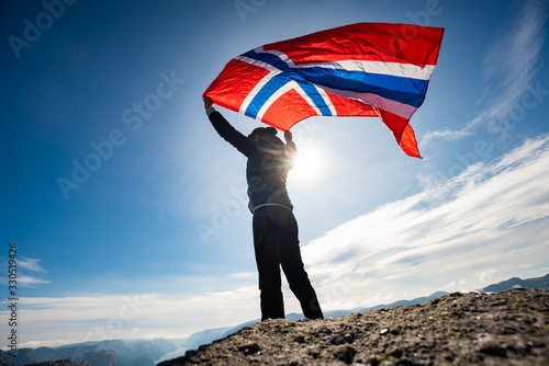 Woman with a waving flag of Norway on the background of nature photo