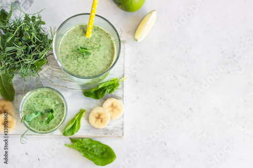 Green smoothie with spinach, banana, lime, mint and young sprout microgreen on light grey stone background.