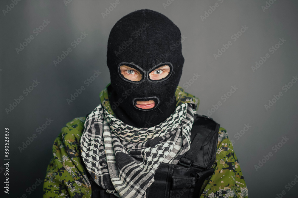 A man in camouflage and bullet proof vest, with a balaclava on his head. A special unit soldier, a modern warrior. A photo on a gray background, studio. A man in camouflage and bullet proof vest, with a balaclava on his head. A special unit soldier, a modern warrior. A photo on a gray background, studio.
