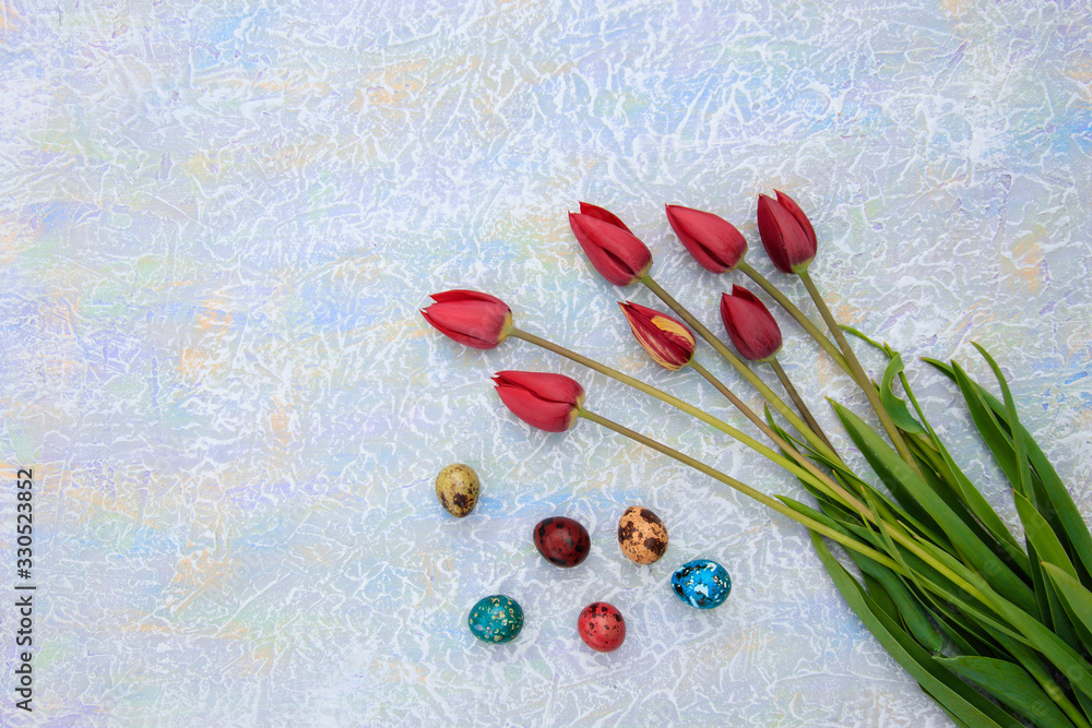 Easter eggs of different colors and a bouquet of tulips on a concrete multi-colored table with copyspace. Easter eggs of different colors and a bouquet of tulips on a concrete multi-colored table with copyspace.