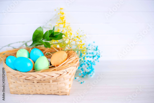 Easter eggs in a basket on a white wooden table. Copy space.