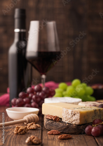Glass and bottle of red wine with selection of various cheese on the board and grapes on wooden background. Blue Stilton, Red Leicester and Brie Cheese and bowl of nuts.