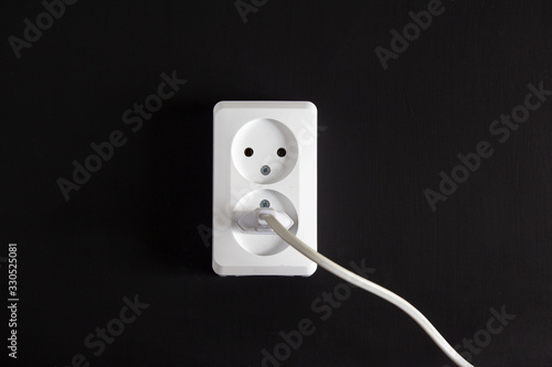 Socket with two plugs on a black wall with a plug in.