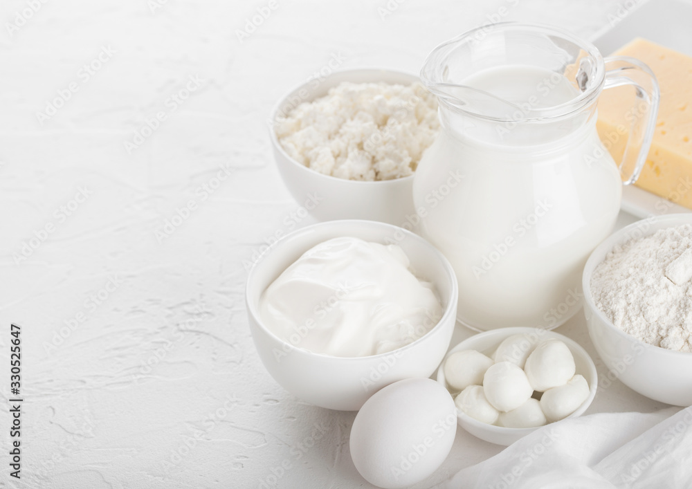 Fresh dairy products on white table background. Glass jar of milk, bowl of sour cream, cottage cheese and baking flour and mozzarella. Eggs and cheese. Fresh dairy products on white table background. Glass jar of milk, bowl of sour cream, cottage cheese and baking flour and mozzarella. Eggs and cheese.