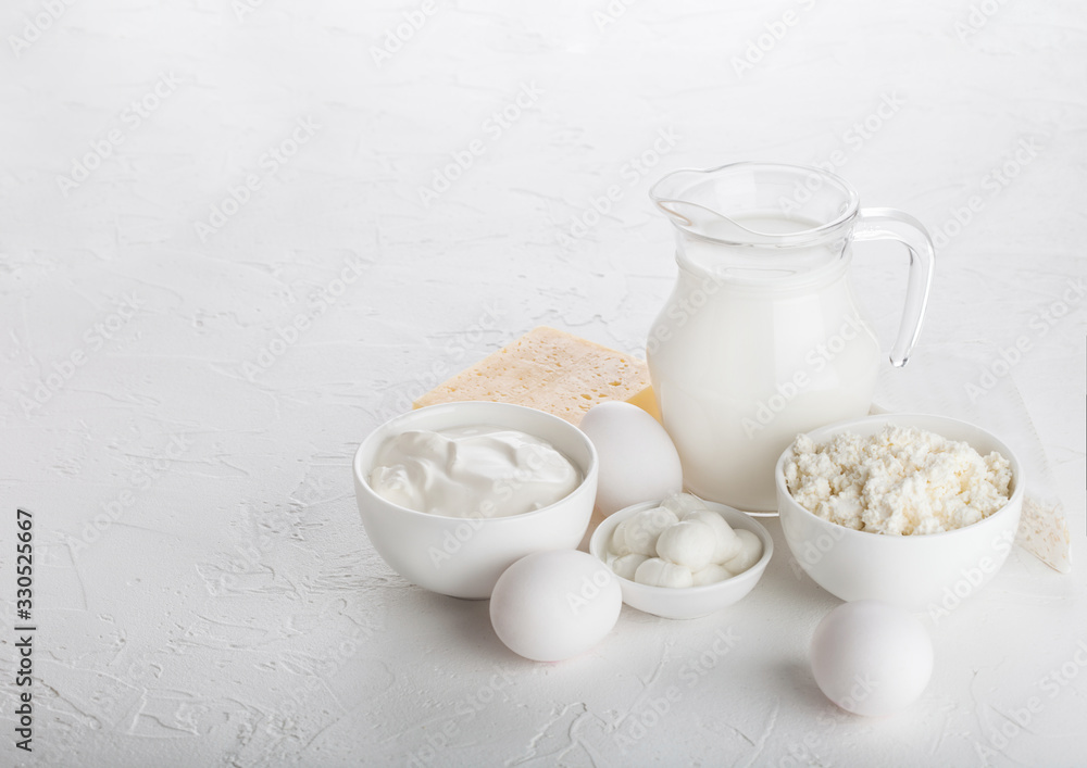 Fresh dairy products on white table background. Glass jar of milk, bowl of sour cream and cottage cheese and mozzarella. Eggs in and cheese. Space for text Fresh dairy products on white table background. Glass jar of milk, bowl of sour cream and cottage cheese and mozzarella. Eggs in and cheese. Space for text
