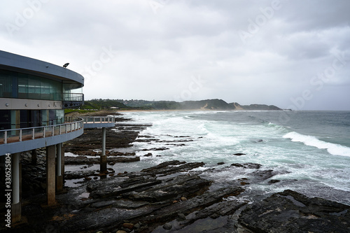 Waves crash in over a rocky coastline with building in foreground