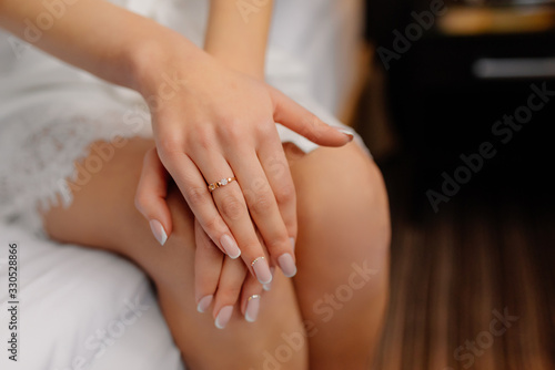 Wedding morning preparation. Happy bride holds hands on her knees shows engagement ring