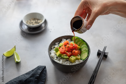 Behang woman's hand pours soy sauce in a bowl with salmon, rice, avocado and cucumber