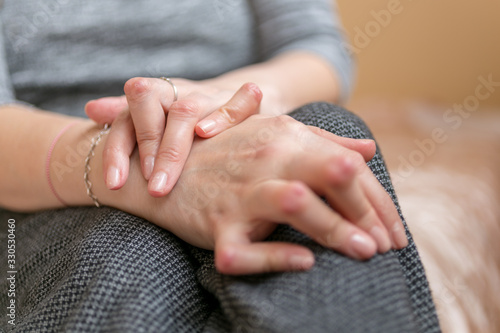 Young woman having rheumatoid arthritis takes a rest sittinng on the couch. Hands and legs are deformed. She feels pain. Selected focus. photo