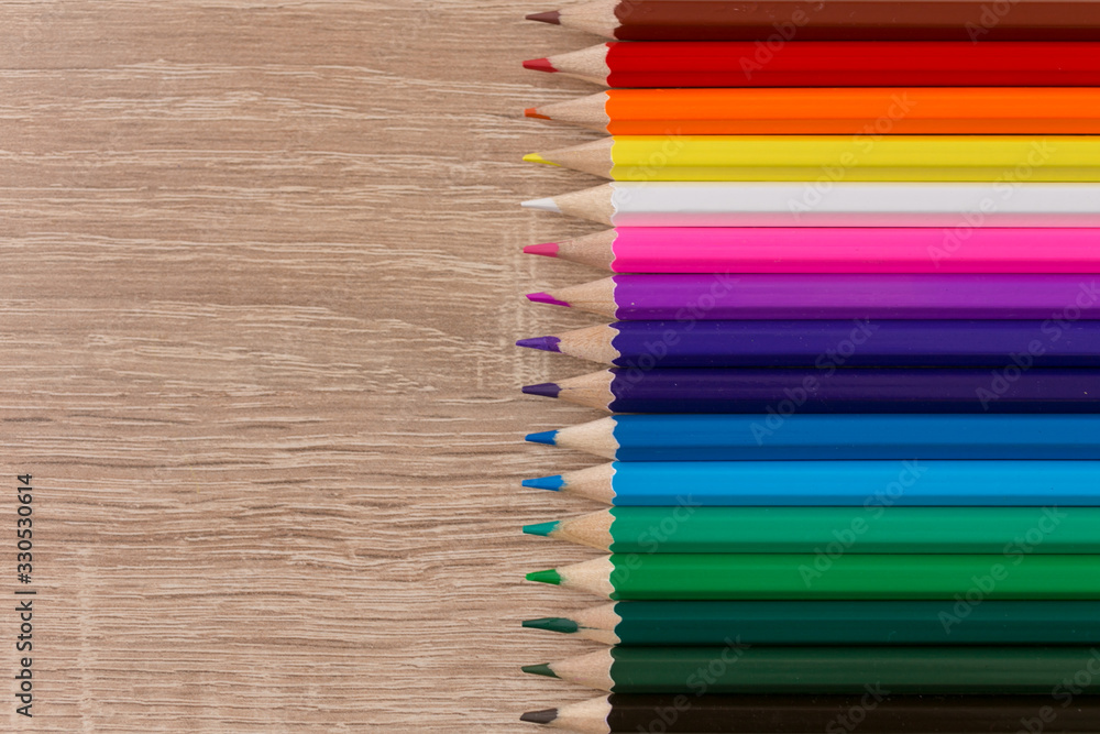 A number of colored pencils in a row on wooden background. Colorful photograpphy.