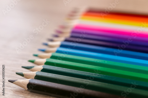 A number of colored pencils in a row on wooden background. Colorful photograpphy. Selected focus on black.