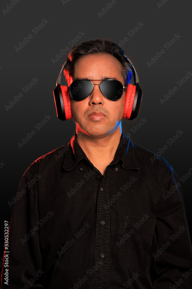 Indian man with sunglasses and wireless headphones on grey background Indian man with sunglasses and wireless headphones on grey background