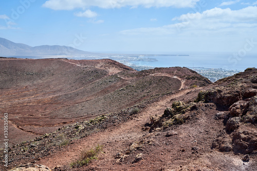 Der Vulkan Montana Roja de Playa Blanca mit einer Höhe von 194m auf der Südwestspitze der Kanareninsel Lanzarote und im Hintergrund die Feuerberge