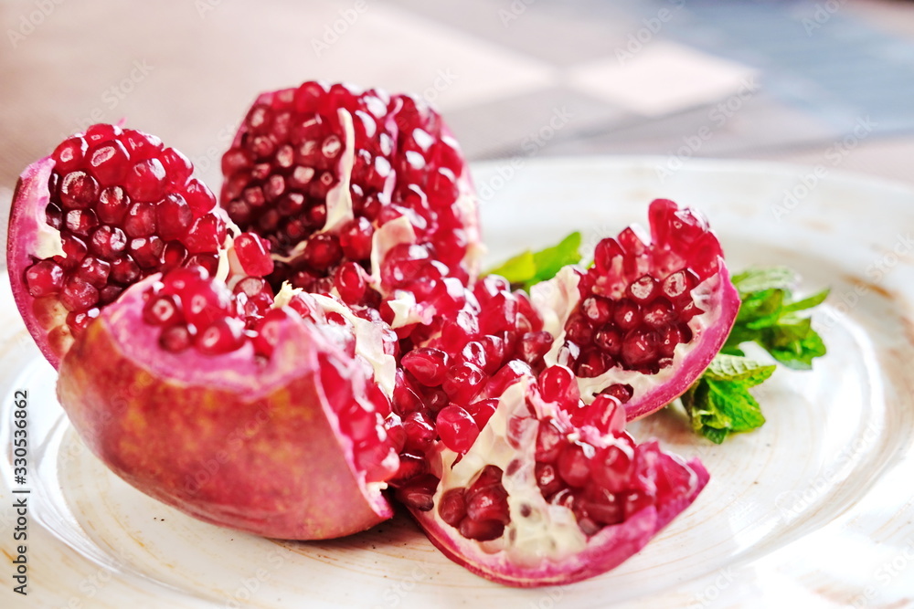 a red pomegranate cut into pieces is lying on a white plate decorated with mint sprigs. a red pomegranate cut into pieces is lying on a white plate decorated with mint sprigs.