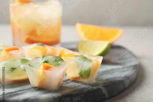 Ice cubes with orange and mint on light grey table, closeup